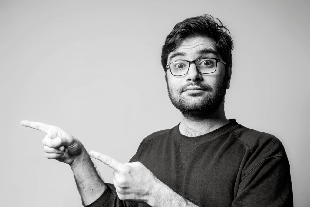 Black and white portrait of a confident man gesturing with both hands, indicating direction.
